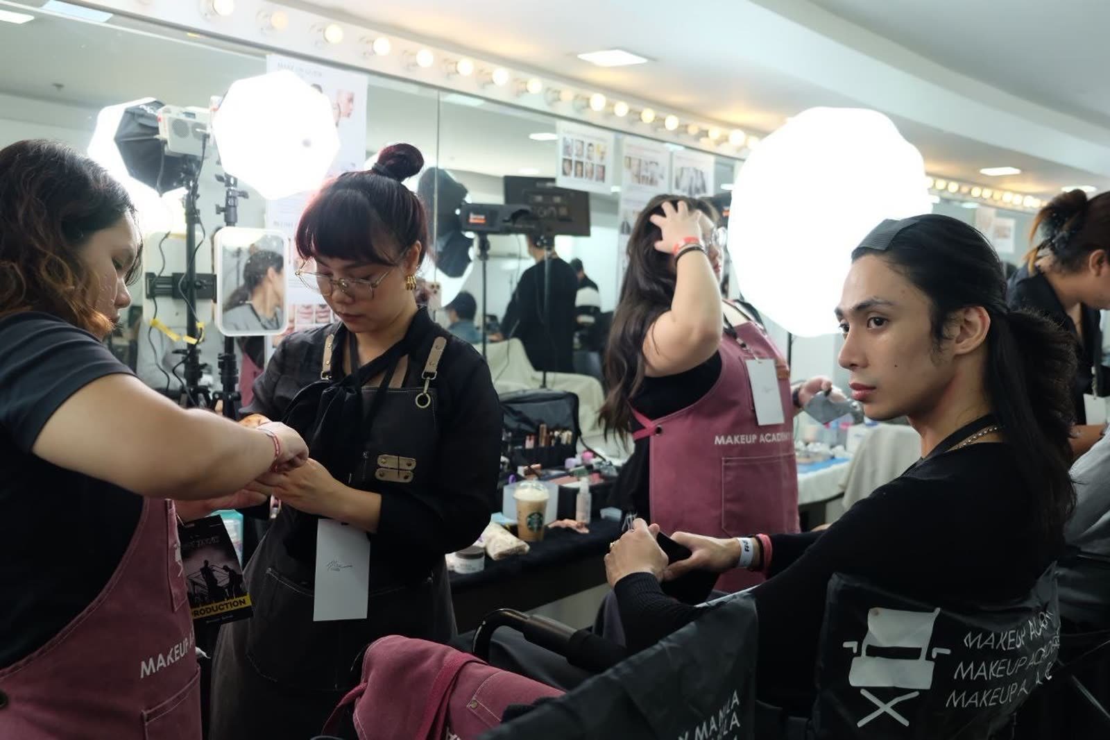 Makeup Academy Manila students working backstage at lit vanity mirrors during a production.